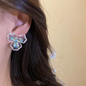 Detailansicht eines floralen Zirkonia-Ohrrings am Ohr mit blauen Kristallakzenten.