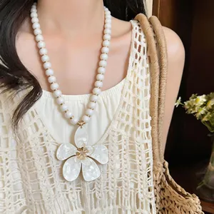 Detailed shot of a white flower pendant necklace with beads on a vacation-style outfit.