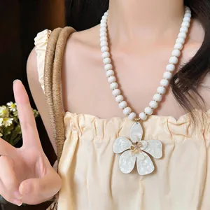 Detail shot of a beach-style white beaded necklace with a large flower pendant on a model