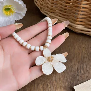 Close-up detail of elegant white beaded necklace with a large flower pendant and gold accents