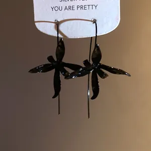 Close-up of black painted metal flower drop earrings on a silver 925 display card