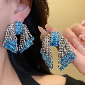 Detail view of oversized sparkling blue and clear rhinestone bow earrings worn on ear