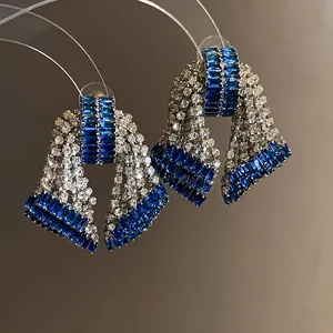 Detailed close-up of oversized bow earrings with blue baguettes and sparkling clear zircons.