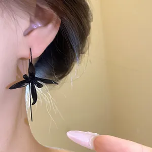Close-up of elegant black painted metal flower pendant drop earrings worn on the ear