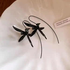 Close-up detail of black metal flower drop earrings on a white shell-textured plate.