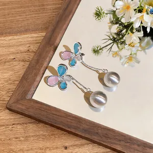 Detail of butterfly stud earrings with silver needles and silver metallic bead tassels.