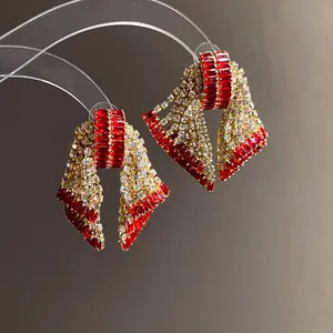 Close-up view of elegant bow-shaped earrings featuring red and clear sparkling zirconia stones.
