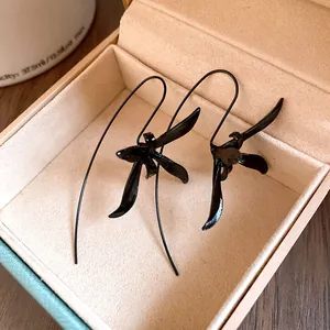 Close-up of elegant black metallic orchid flower drop earrings inside a premium beige velvet box