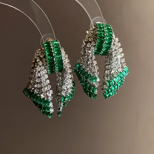 Close-up of emerald and clear zircon encrusted bow-shaped silver needle earrings