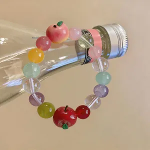 Close-up of a colorful beaded bracelet with resin apple and peach charms on a bottle