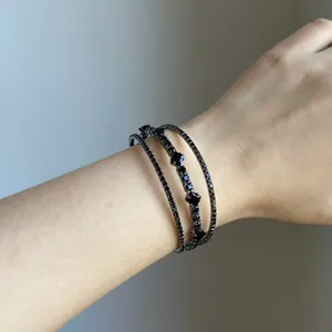 Dettaglio ravvicinato di un bracciale rigido multistrato nero con diamanti sul polso
