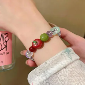 Close-up of a colorful beaded bracelet featuring a red resin apple charm on a wrist