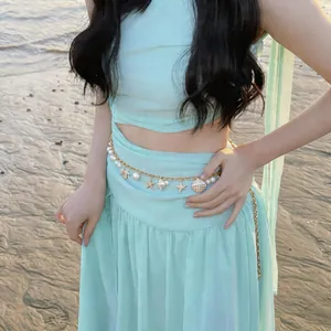 Detailed view of a golden pearl waist chain featuring starfish and shell charms at the beach