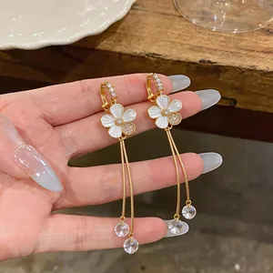Close-up of elegant white enamel flower ear clips with zircon and long gold tassels
