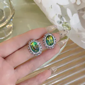 Close-up of vintage court style oval earrings with iridescent green resin and rhinestones