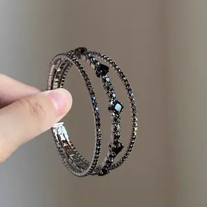 Dettaglio ravvicinato di bracciale elastico multistrato con strass neri e motivi a rombi
