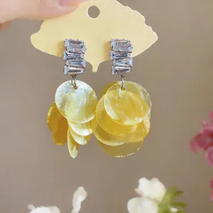 Detailed view of geometric zircon earrings with layered yellow shell disc tassels.