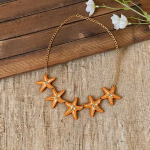 Close-up view of five orange enamel starfish pendants on a golden chain necklace.