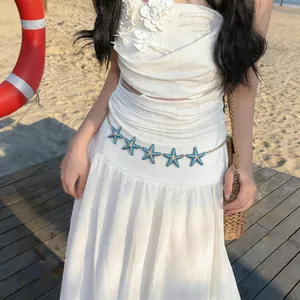 Detail of blue enamel starfish waist chain styled with a white summer dress on a beach