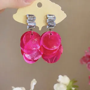 Close-up of bright pink shell earrings with geometric zircon studs in a vacation style