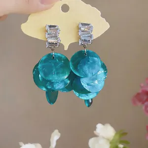 Detail view of turquoise shell-pattern disc tassel earrings with sparkling zircon studs.