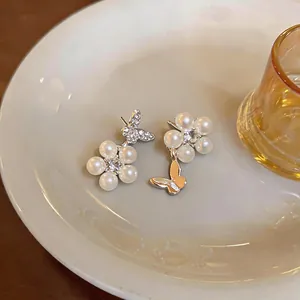 Close-up of elegant mismatched French style zircon butterfly and pearl flower earrings