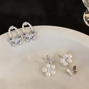 Detailed view of elegant zircon butterfly and pearl earrings set on a ceramic plate.