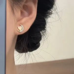 Close-up view of a dainty gold moon and cat's eye heart stud earring worn on a model's ear.