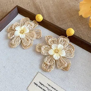 Close-up detail of Bohemian raffia flower earrings with yellow woven studs and white centers