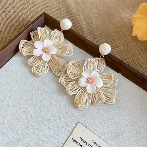 Close-up of woven raffia flower earrings with delicate fabric petals and gold center.