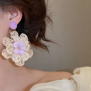 Detailed view of a Bohemian raffia flower earring with purple accents on a model.