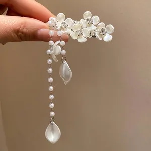 Elegant white flower hair clip with pearl tassels and rhinestones on a warm beige background
