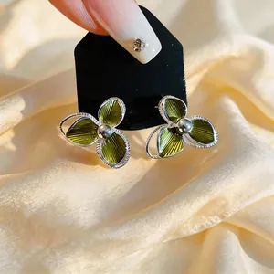 Elegant green enamel flower stud earrings with silver needles on a soft satin background