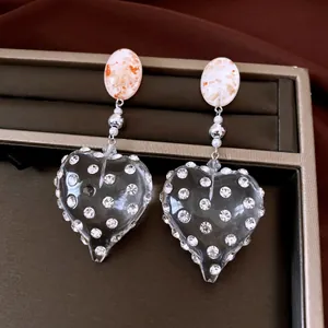 Dettaglio ravvicinato di orecchini pendenti a cuore in resina vintage con strass lucenti
