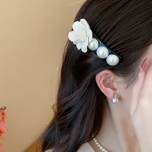 Detailed view of an elegant French fabric flower and pearl hair clip on dark hair