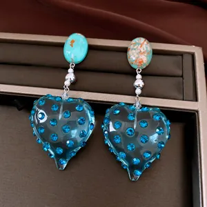 Dettaglio di orecchini a cuore in resina blu con strass scintillanti e perni vintage.