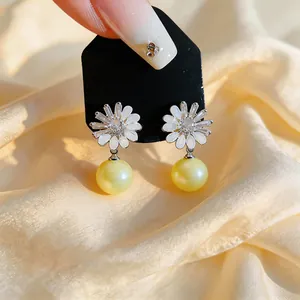 Detailed view of elegant floral stud earrings with white enamel petals and yellow pearls