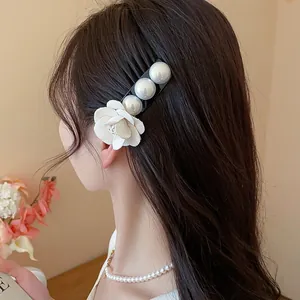Detail view of an elegant fabric flower and pearl hair fork worn on dark wavy hair.