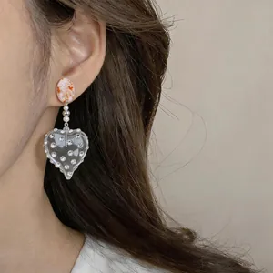 Dettaglio di orecchini vintage a cuore in resina con strass indossati da una modella