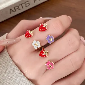 Detail showing colorful enamel strawberry and flower open rings on a female hand