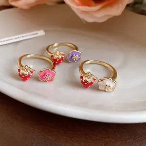 Detailed view of three enamel strawberry and flower open rings on a white plate