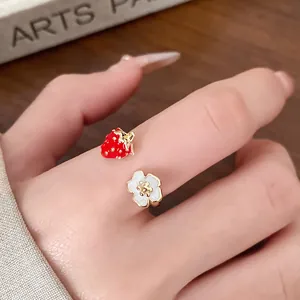 Close-up view of a sweet enamel strawberry and white flower open ring on a finger.