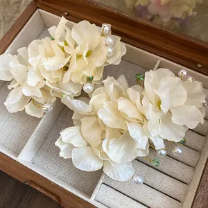 Détail de barrettes fleurs en tissu blanc cassé avec perles dans un coffret bois.