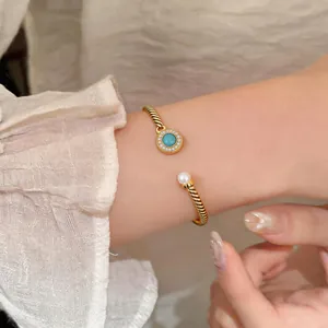 Detail of a gold-plated twisted cable cuff bracelet with turquoise and pearl accents.