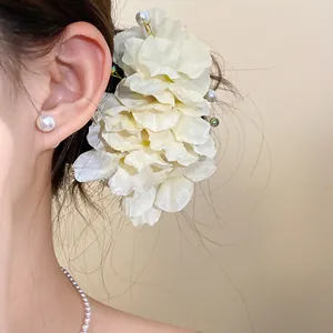 Détail d'une pince à cheveux élégante en fleur de tissu blanc avec perles et cristaux.