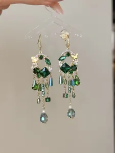 Close-up of green faceted glass gemstone earrings with beaded tassels and pearls.