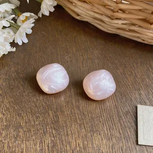 Dettaglio ravvicinato di orecchini a lobo quadrati rosa con texture perlacea e finitura lucida