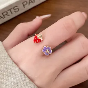 Macro detail showing a delicate gold enamel open ring with strawberry and purple flower charm