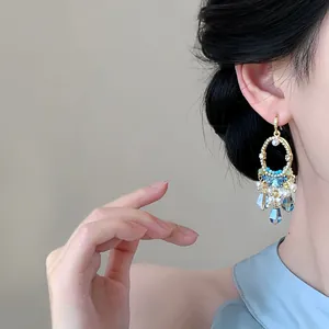 Detailed close-up of ethnic style gold-tone tassel earrings with blue beads on a model
