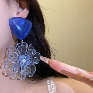 Large blue triangle and transparent resin flower drop earrings worn by a model.